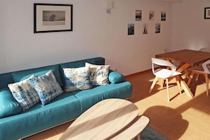 A modern living room with a teal sofa, wooden dining table, and white chairs.