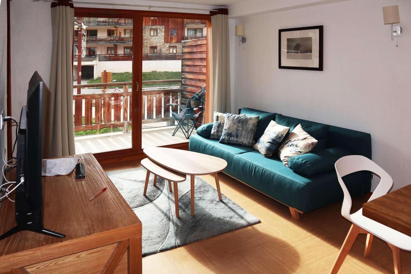 Een moderne woonkamer met een blauwgroene bank, een houten salontafel en een televisie op een houten standaard.