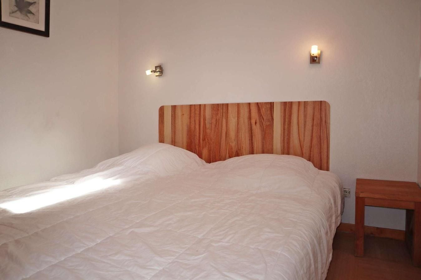 A single bed with a wooden headboard, two wall-mounted lights, and a small wooden nightstand.