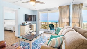 A living room with a ceiling fan, a flat-screen TV, a sofa with cushions, a coffee table, and a view of the ocean through large sliding glass doors. - ✨FAB Gulf Views~Pool~Beach Svc~2BR Destin on the Gulf 402 (Destin)