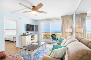 Relax in this serene space with a large flat-screen TV, comfortable sofa, and sliding glass door leading to an ocean view balcony.