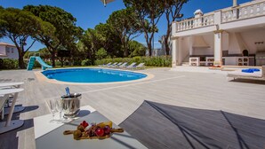 A poolside area with a pool, lounge chairs, a table with a bottle and glasses, and a buffet table with fruits. - Portuguese mansion close to marina, golf and beach. (Quarteira)