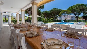 An outdoor dining area with a pool view, white chairs, and a wooden table set for a meal. - Portuguese mansion close to marina, golf and beach. (Quarteira)