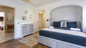 Un dormitorio moderno con una cama grande, un armario empotrado, un baño con lavamanos y espejo, y un pasillo que conduce a otra habitación.