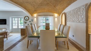 A dining area with a glass table, white chairs, and a stone accent wall. - Portuguese mansion close to marina, golf and beach. (Quarteira)