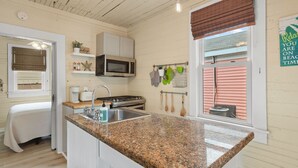 A kitchen with granite countertops, a microwave, a stove, and a window with a view of a pink house.