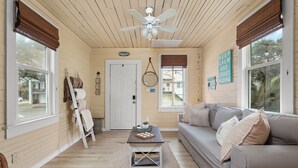 A cozy living room with a wooden ceiling, a ceiling fan, a gray sofa, and a coffee table with decorative items.