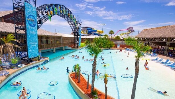 A large pool area with multiple water slides, palm trees, and lounge chairs.