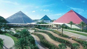 A large building with a pyramid-shaped structure, surrounded by landscaped gardens and palm trees.
