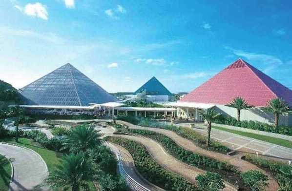 Three pyramidal structures surround lush gardens with palm trees and a curved pathway.