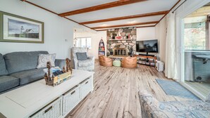 Un salon chaleureux avec un plafond en bois, une cheminée en pierre, un téléviseur et une grande fenêtre.