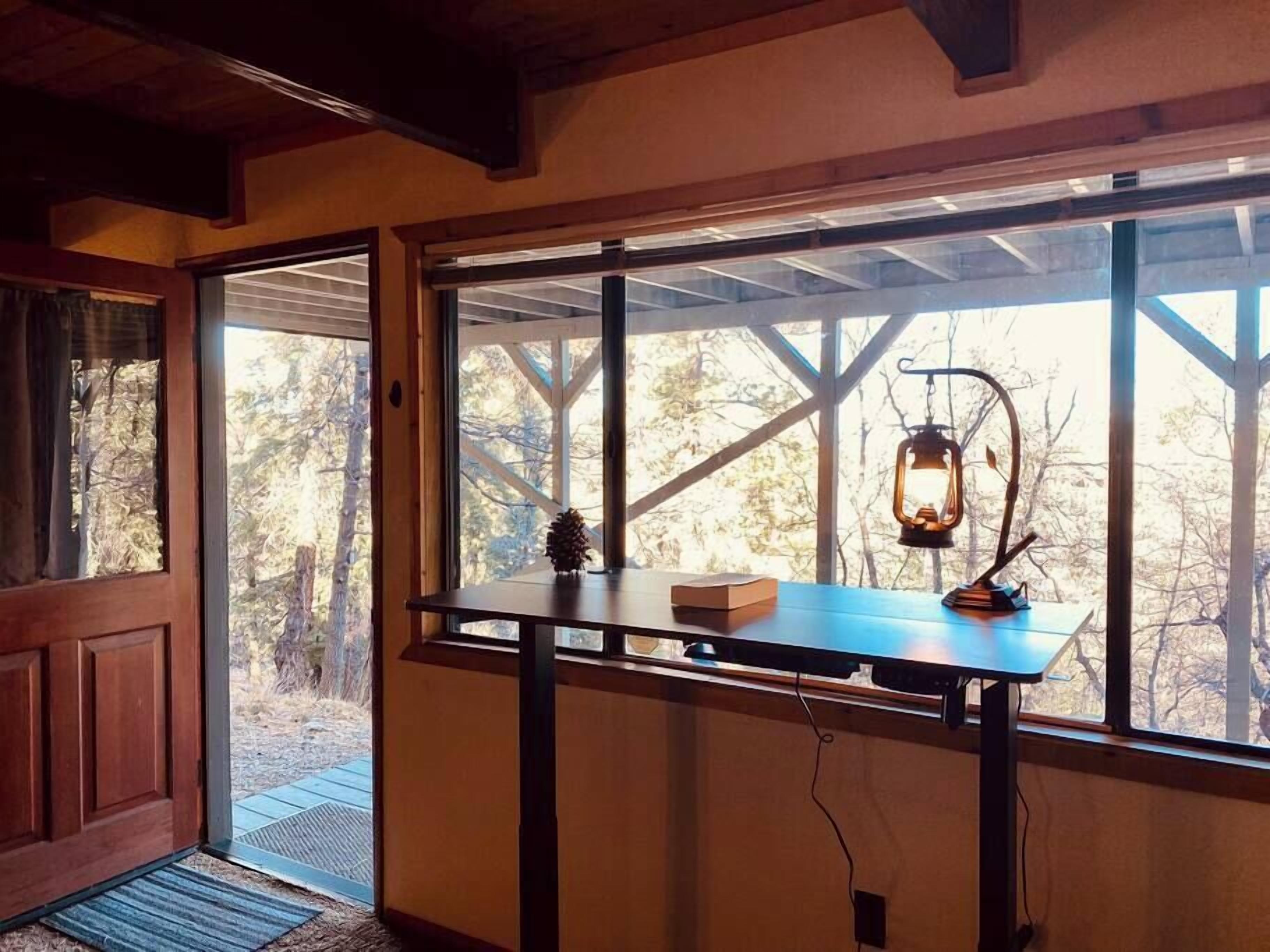 Ein Zimmer mit Holztür, einem Fenster mit Blick auf Bäume, einem Tisch mit Laterne und einer Kiefernzapfen-Dekoration.