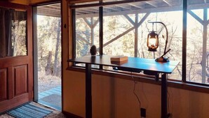 Ein Zimmer mit Holztür, einem Fenster mit Blick auf Bäume, einem Tisch mit Laterne und einer Kiefernzapfen-Dekoration.