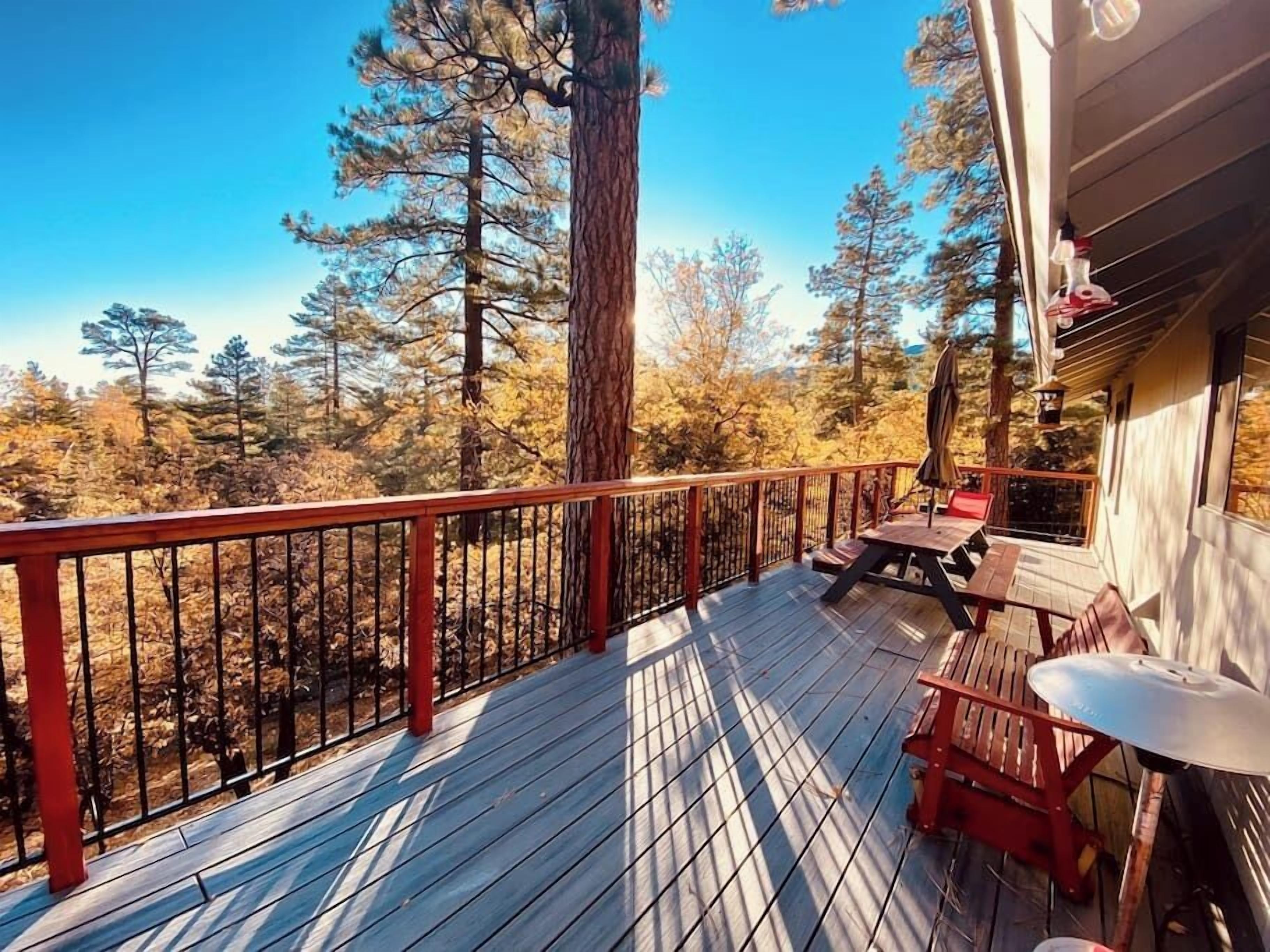 A wooden deck with a railing, a table, and chairs, overlooking a forested area.
