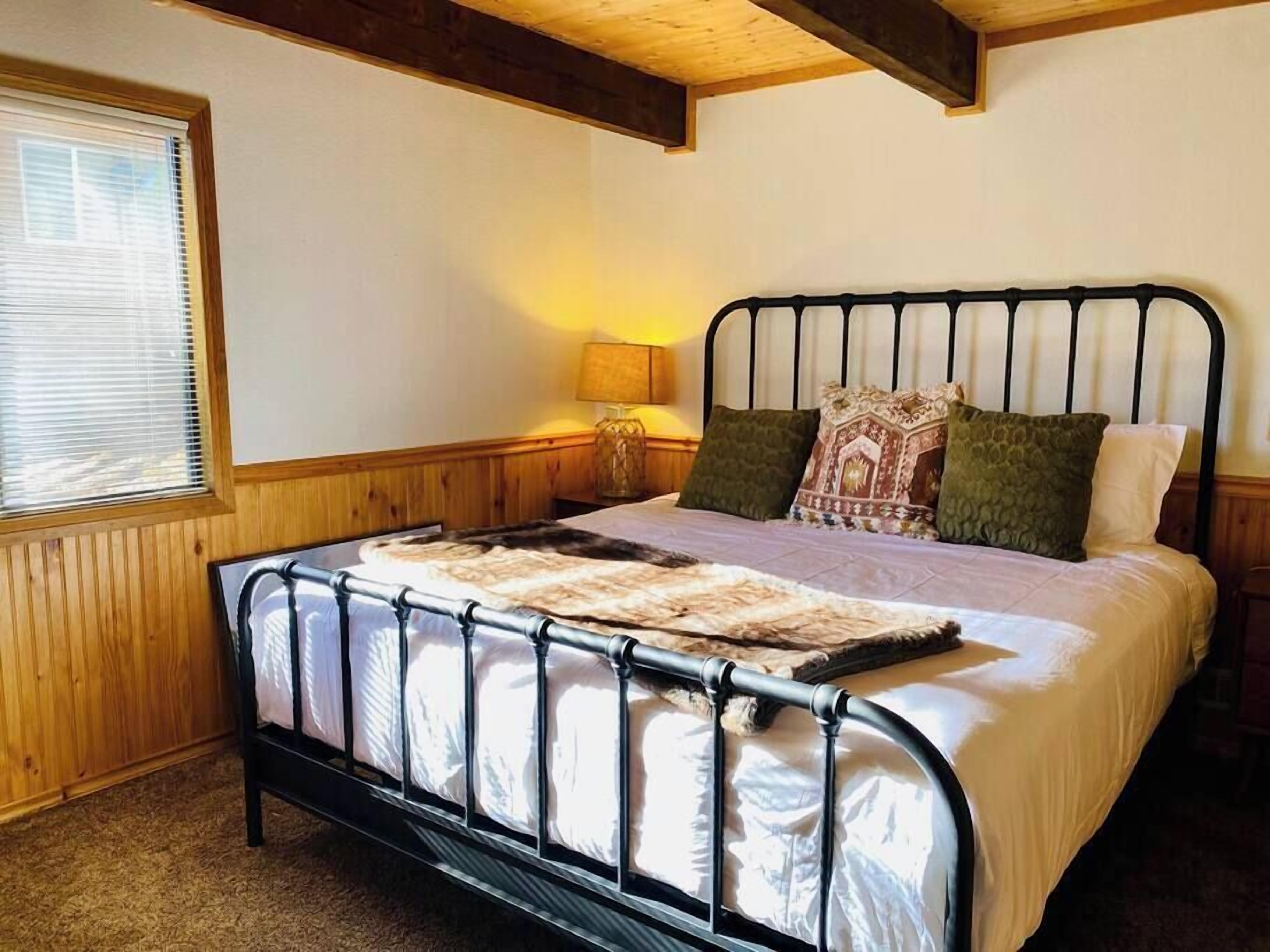 Een bed met een metalen frame, een houten hoofdbord en een bedsprei met een patroon.