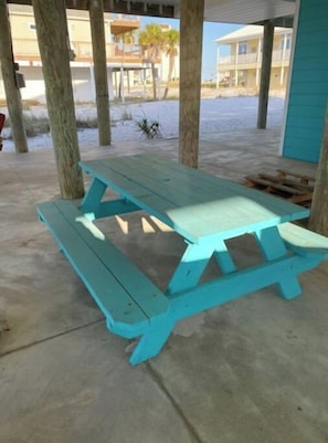 A turquoise picnic table with benches, set on a concrete floor under a covered area with wooden pillars.