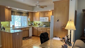A kitchen with wooden cabinets, a microwave, a refrigerator, and a dining area with a lamp and a chair. - Spacious Lake Almanor West Getaway - Enjoy Everything the Lake Has to Offer  (Chester)