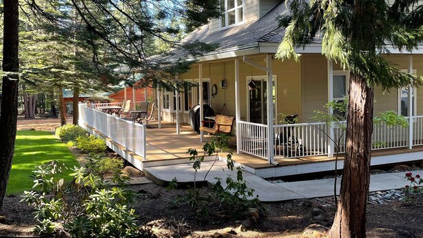 A two-story house with a porch, surrounded by trees and a well-maintained lawn. - Spacious Lake Almanor West Getaway - Enjoy Everything the Lake Has to Offer  (Chester)