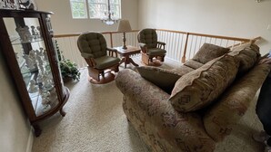A cozy living room with a high ceiling, a wooden chair, a sofa, and a glass cabinet with figurines. - Spacious Lake Almanor West Getaway - Enjoy Everything the Lake Has to Offer  (Chester)