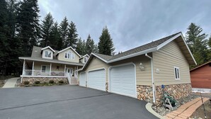 A two-story house with a covered porch, stone foundation, and two garage doors. - Spacious Lake Almanor West Getaway - Enjoy Everything the Lake Has to Offer  (Chester)