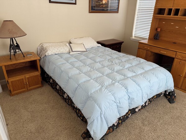 A bedroom with a light blue quilted bedspread, a wooden nightstand with a lamp, a small wooden dresser, and a framed picture on the wall. - Spacious Lake Almanor West Getaway - Enjoy Everything the Lake Has to Offer (Chester)