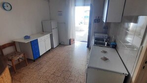 Eine kleine Küche mit weißen Schränken, einem Kühlschrank, einer Spüle und einem Stuhl.