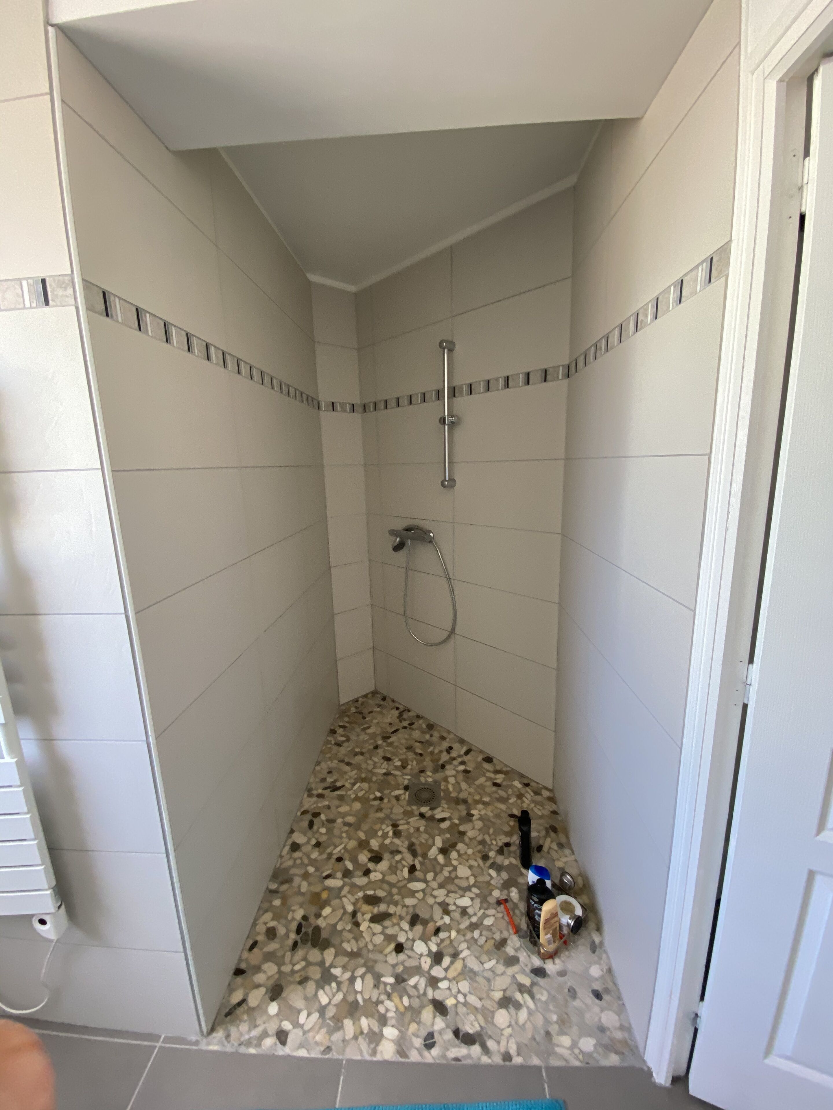 A small, tiled shower room with a pebble-patterned floor and a showerhead.