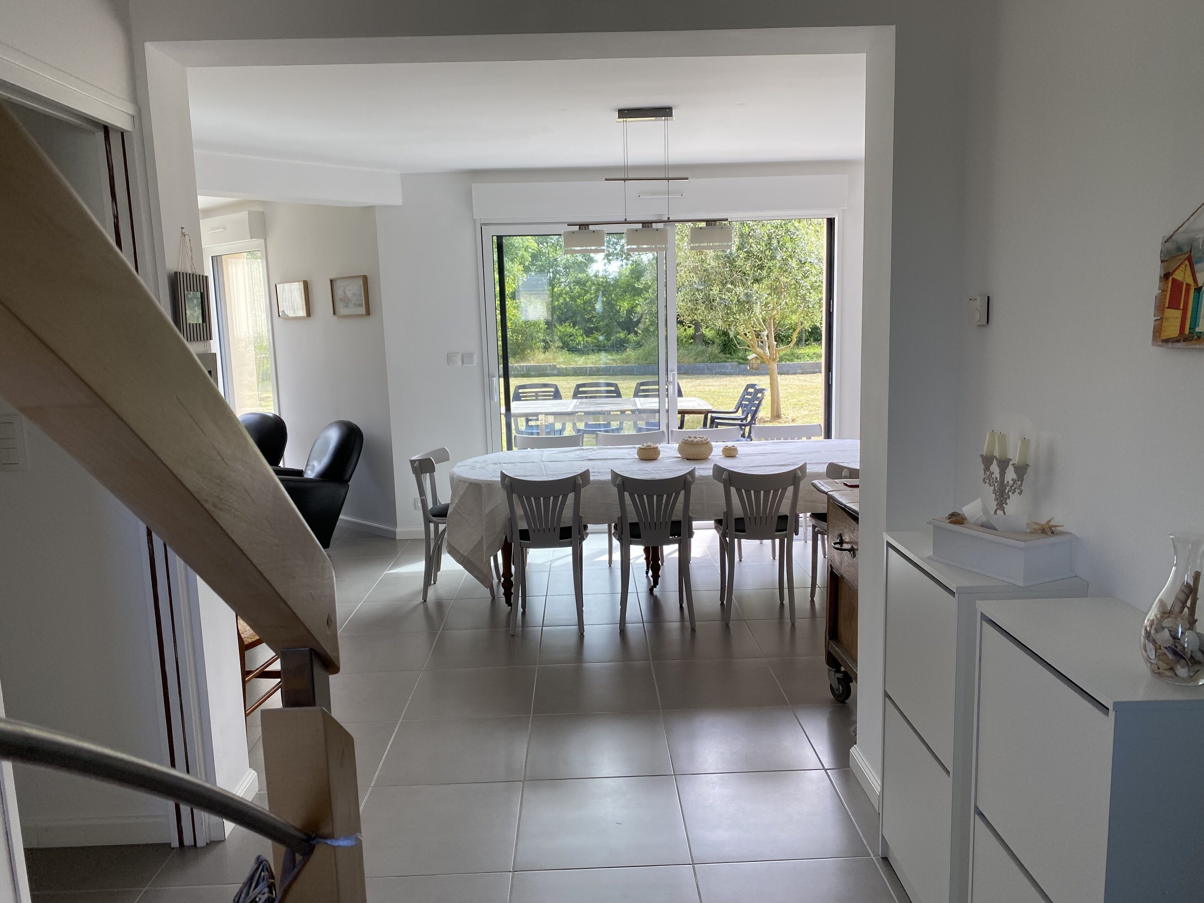 Une cuisine moderne avec des meubles blancs, un coin repas doté d’une table ronde et de chaises, et une vue sur l’extérieur grâce à de grandes fenêtres.