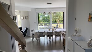 Una cocina moderna con armarios blancos, un comedor con una mesa redonda y sillas, y vistas al exterior a través de amplias ventanas.