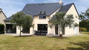 Una casa moderna de dos pisos con techo plano, grandes puertas correderas de vidrio y un patio con mobiliario exterior.
