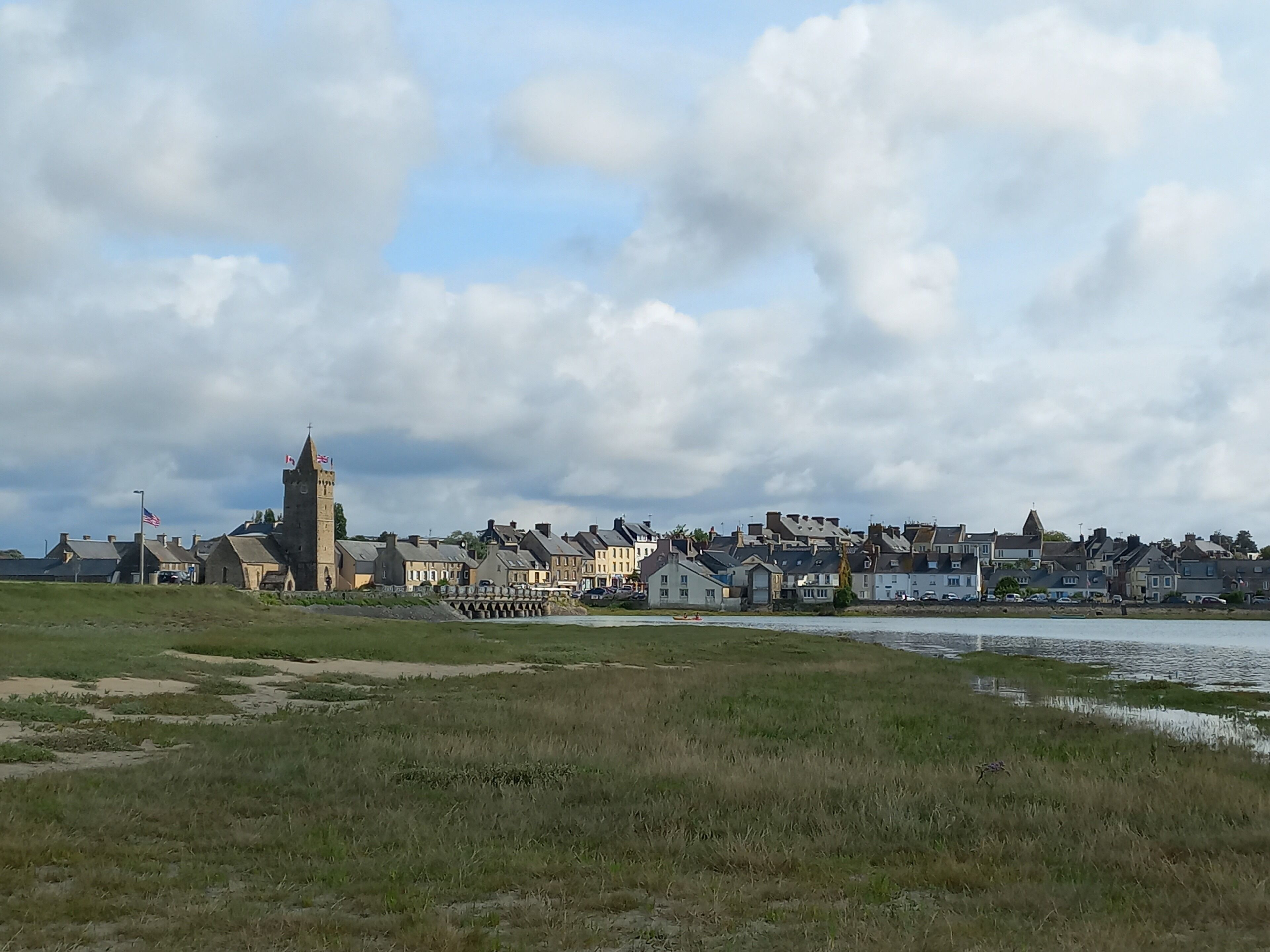 A coastal town with historic buildings, a prominent church tower, and a river.