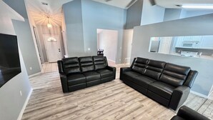 A modern living room with a black leather sofa, a dining area, and a kitchen in the background. - 4-bedroom oasis  in Navarre with enclosed heated  pool (Navarre)