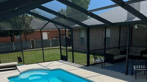 A rectangular swimming pool with clear blue water, surrounded by a covered patio area with chairs and a table. - 4-bedroom oasis  in Navarre with enclosed heated  pool (Navarre)