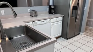 A compact kitchen with a stainless steel sink, a built-in dishwasher, a refrigerator, and a microwave. - 4-bedroom oasis  in Navarre with enclosed heated  pool (Navarre)