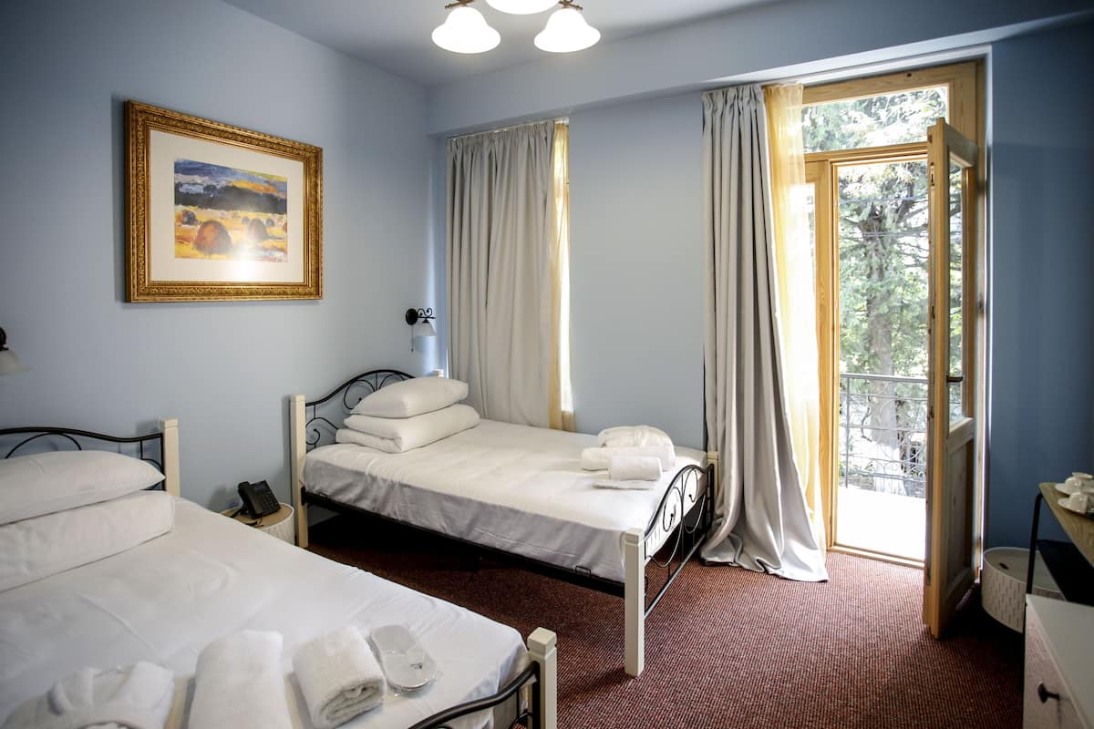 A hotel room with two beds, a painting on the wall, a telephone, and a window with curtains.