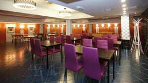 A spacious restaurant with multiple tables and chairs, a chandelier, and a checkered wall pattern.