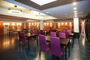 Un restaurant spacieux, doté de nombreuses tables et chaises, d’un lustre et d’un motif à carreaux sur un des murs.