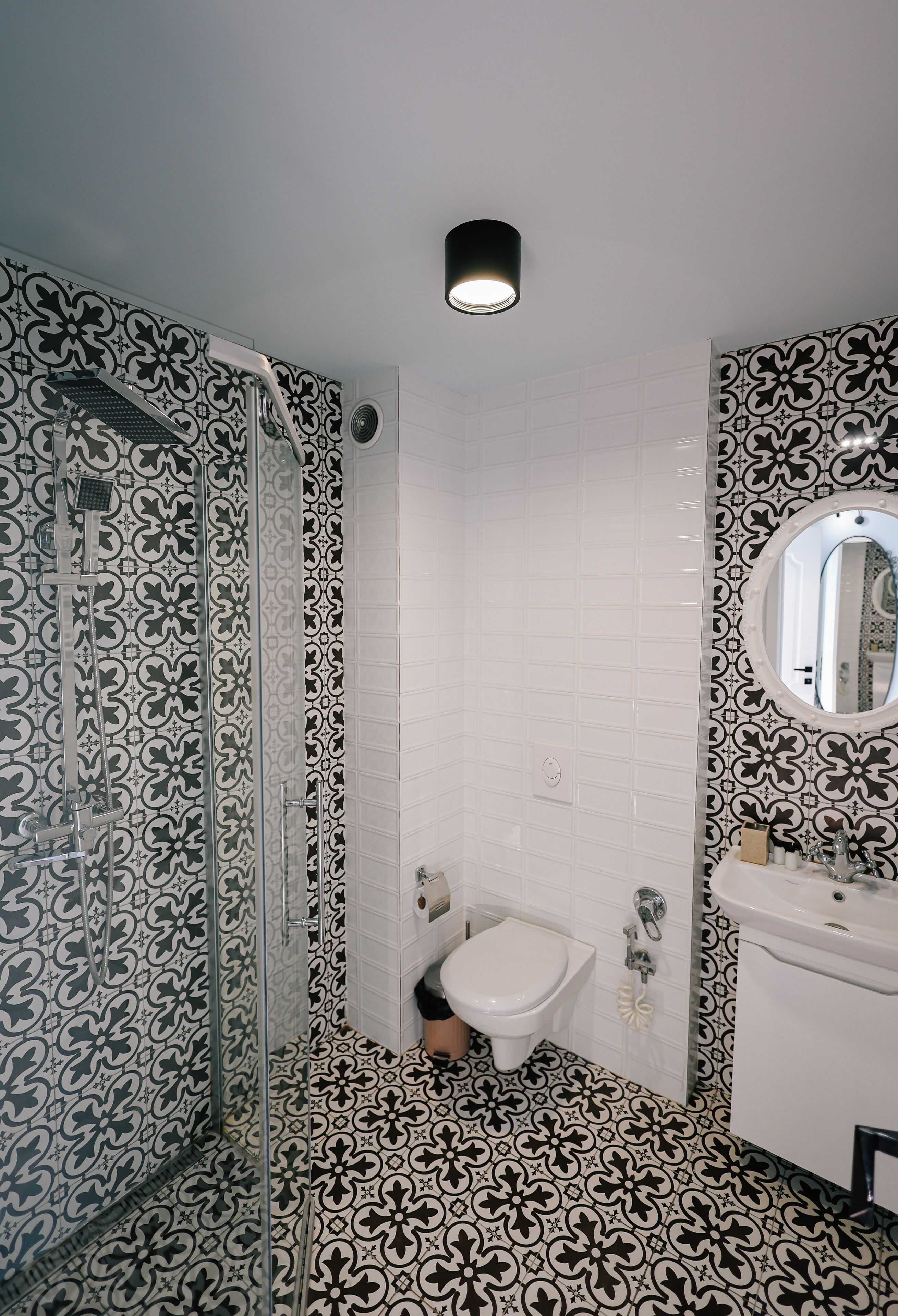 A bathroom with patterned tiles, a glass-enclosed shower, a sink, and a mirror.