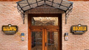 A hotel entrance with a wooden double door, a metal awning, and two signs on either side of the door.