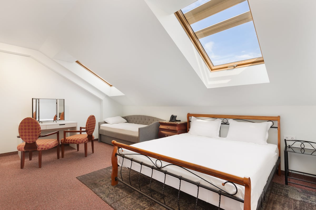 A bedroom with a large bed, a desk, two chairs, a sofa, and a skylight.