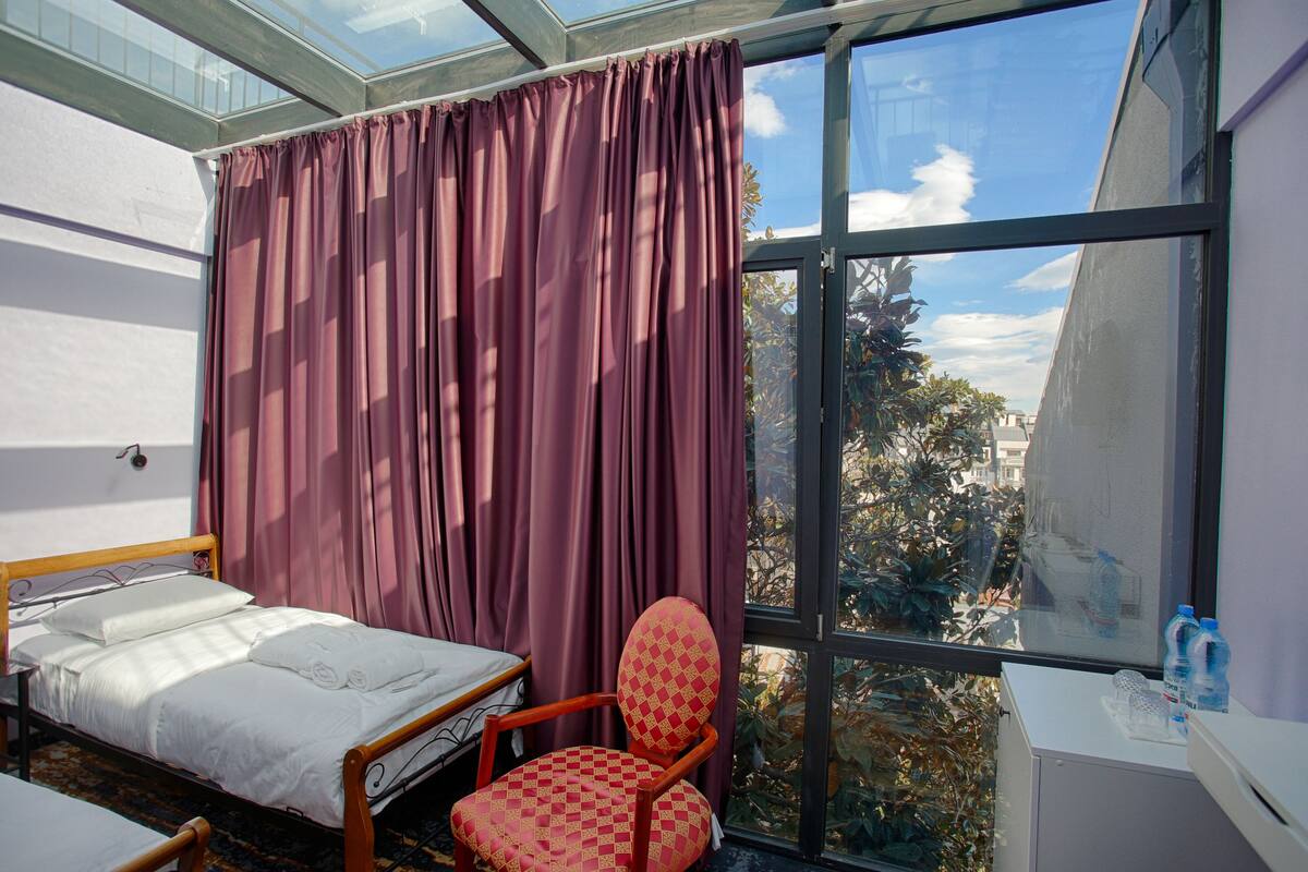 A room with a bed, a chair, and a window with a view of trees and buildings.