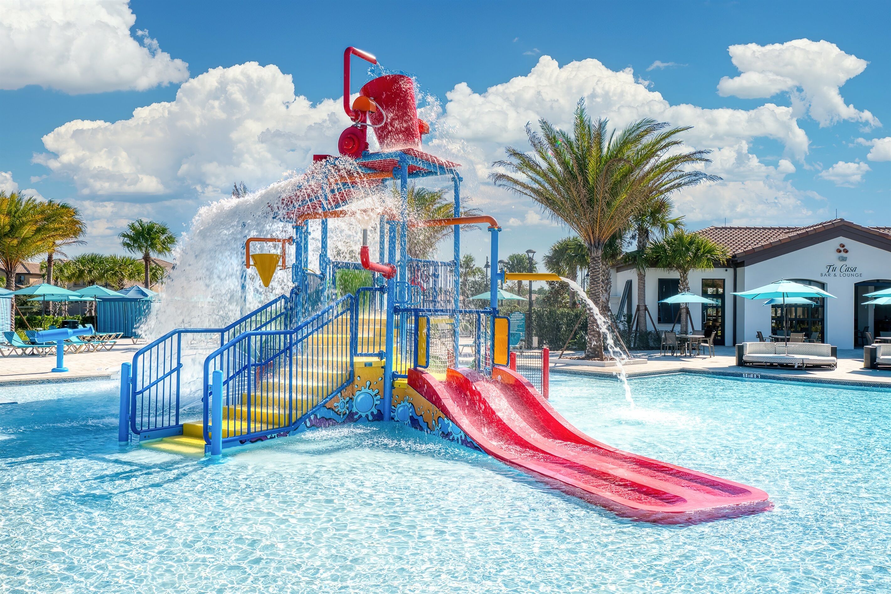 Ein Wasserpark mit einer roten Rutsche, bunten Spielgeräten in Blau und Gelb sowie einem Schwimmbecken.