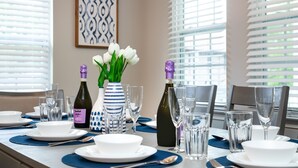 A dining table set with plates, glasses, and wine bottles, with a vase of white flowers in the center.