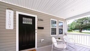 A house with a black front door, a 'WELCOME' sign, and the number 2201. There are two white rocking chairs on the porch.
