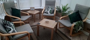 Un coin salon accueillant avec des chaises en bois et une petite table, agrémenté d’un tableau encadré et d’une plante en pot.