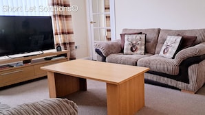 A living room with a sofa, a coffee table, a TV, and a lamp. - Beautiful Three Bedroom Seaside Retreat (Prestonpans)