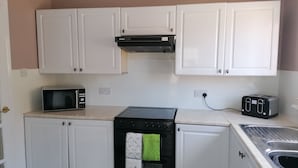 A compact kitchen with white cabinets, a black stove, a microwave, and a toaster. - Beautiful Three Bedroom Seaside Retreat (Prestonpans)