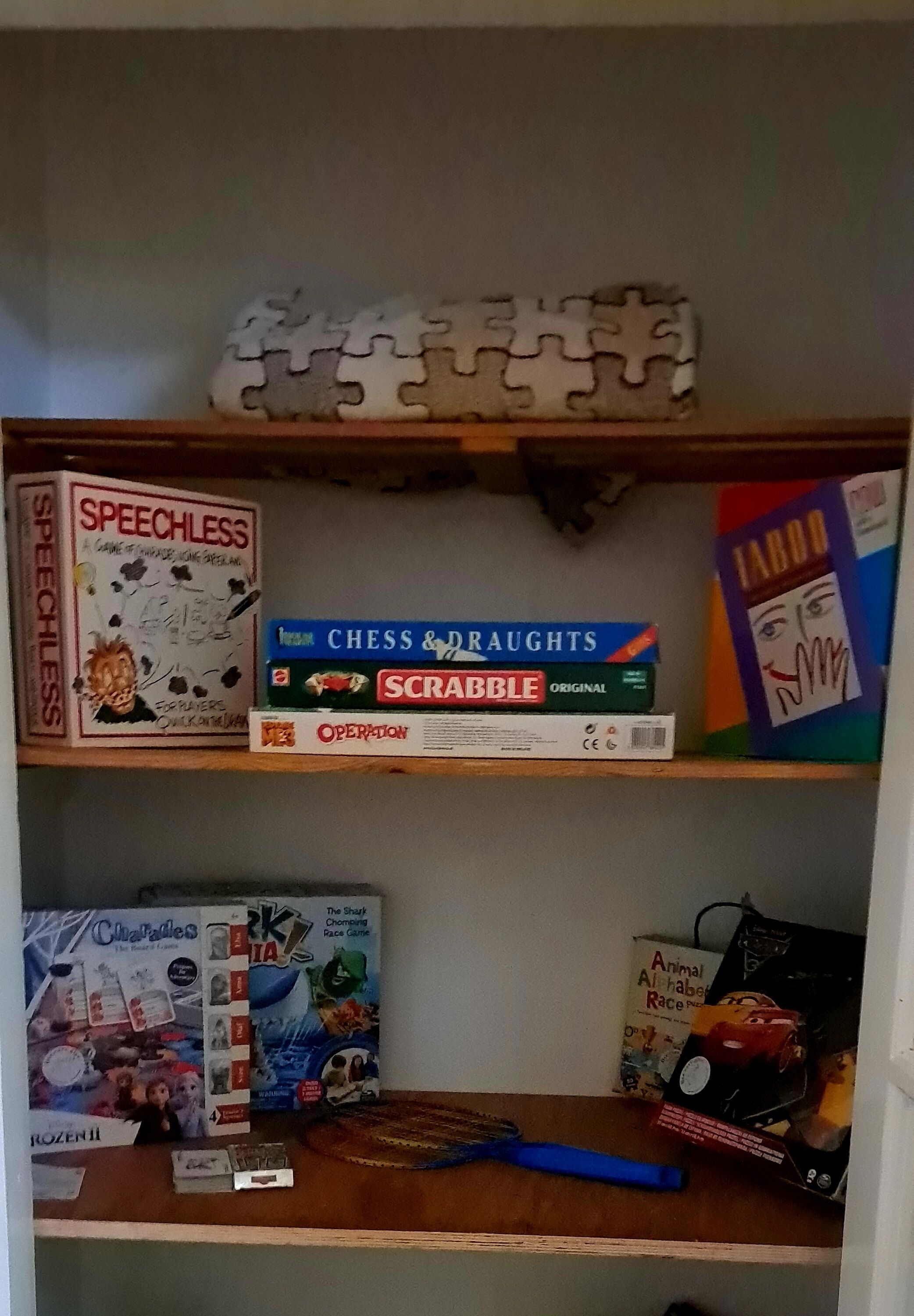 A shelf with various board games including 'Speechless,' 'Chess & Draughts,' 'Scrabble,' and 'Operation.'