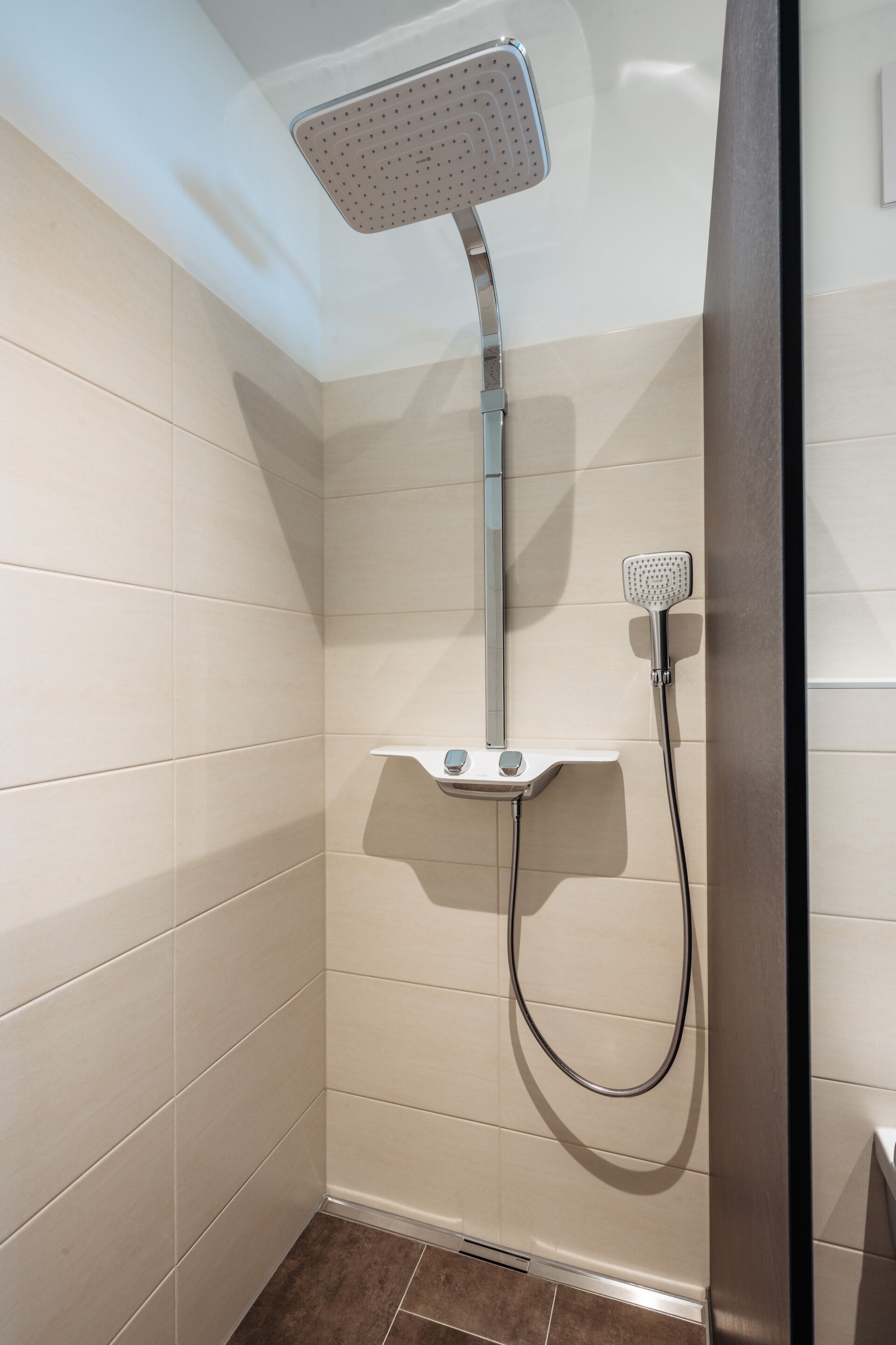 A shower with a handheld showerhead and a fixed overhead showerhead in a tiled bathroom.