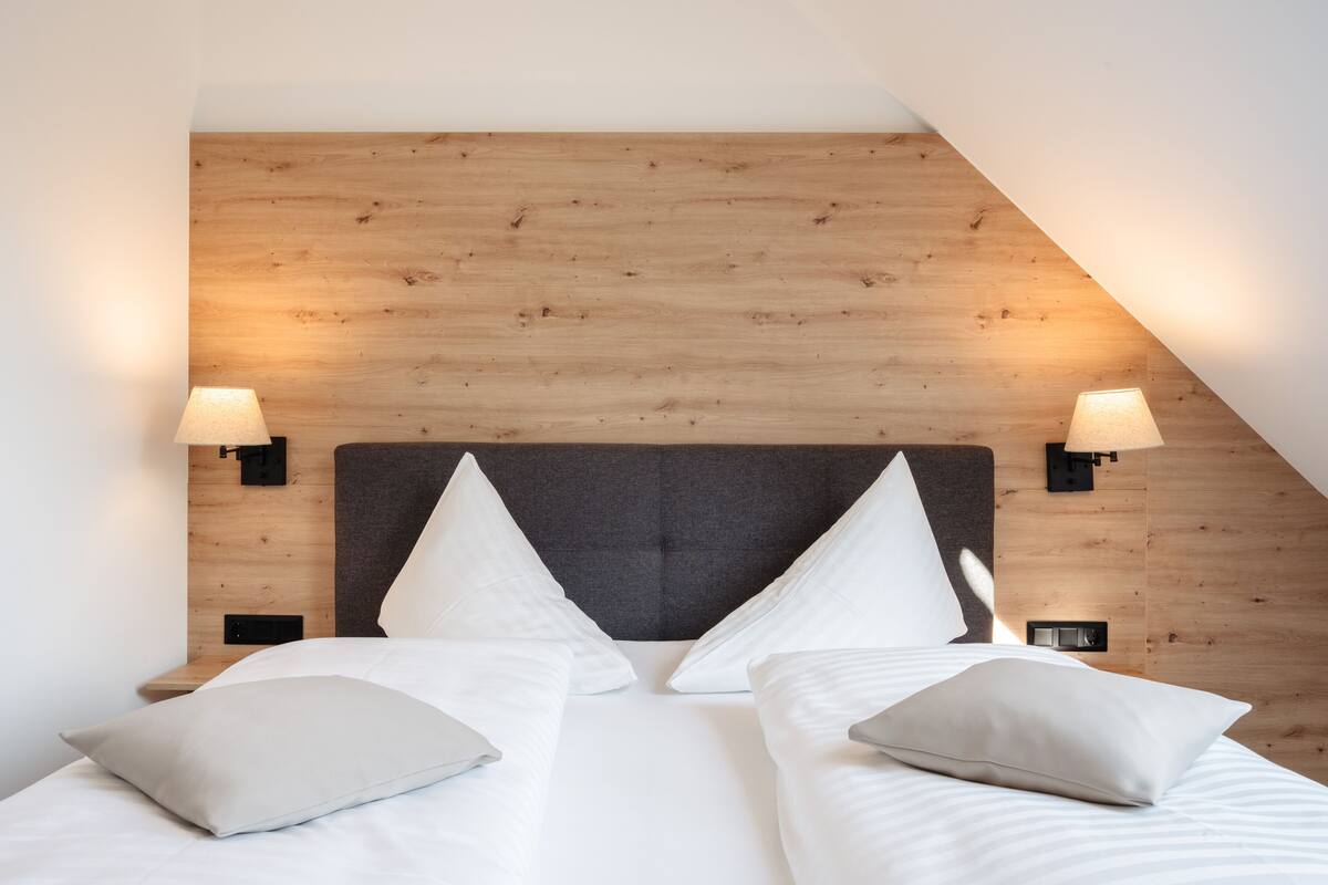 Un dormitorio moderno con cabecera de madera, dos lámparas de noche y una cama bien tendida con almohadas.
